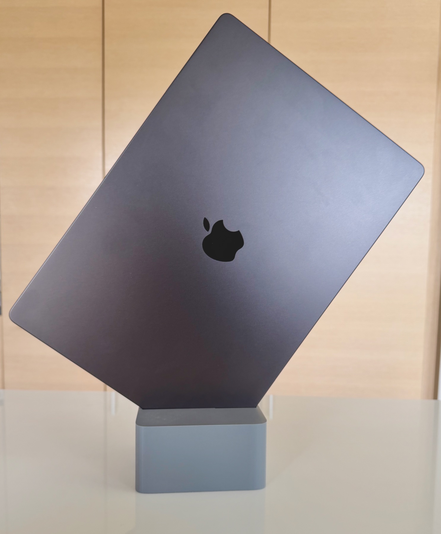 Black MacBook Pro held upright at an angle on a Cubistand against a wood cabinet