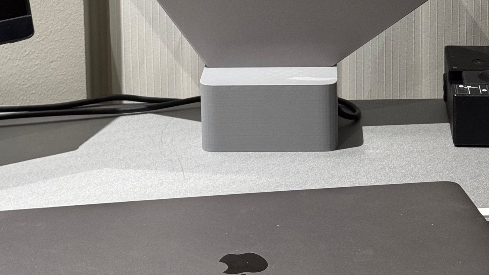 A light gray Cubistand holding a closed MacBook Pro above a crowded desk with another laptop in front